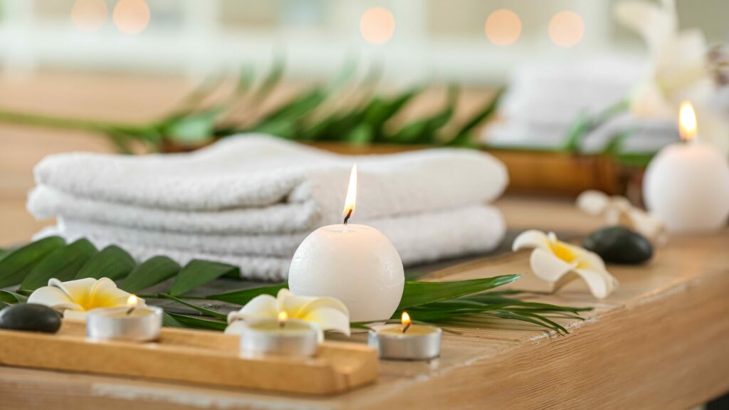 A white towel with greenery, white flowers, and white candles surrounding it.