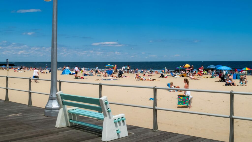 A bench on the boardwalk facing a crowded, sandy beach
