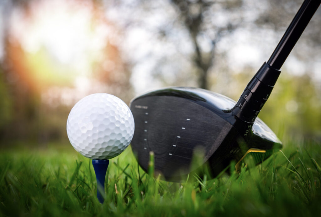 Golf club resting against gold ball on tee