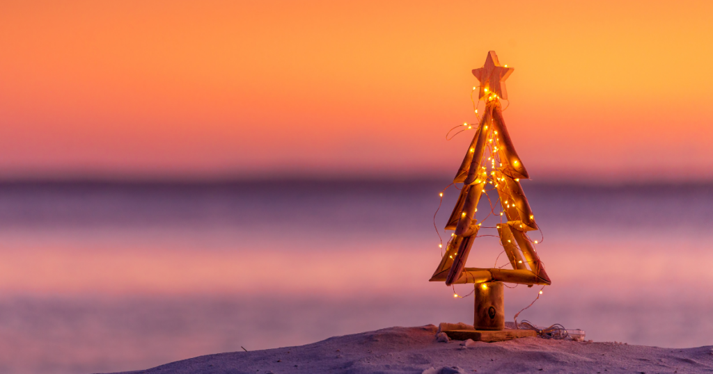 Wooden Christmas tree with lights in the sand near the shore