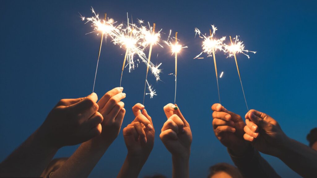 Six hands holding up sparklers in front of the night sky