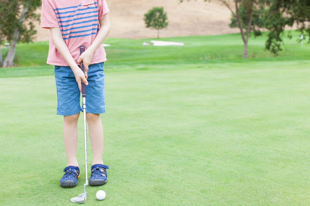 little kid on a mini golf course holding a golf club